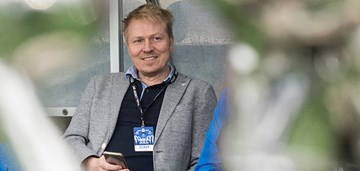 Aki Riihilahti istuu katsomossa hymyillen.