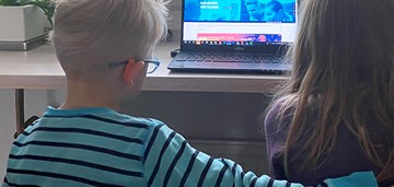 Kaksi lasta istuvat vierekkäin ja katsovat kannettavaa tietokonetta, kuvituskuva.