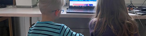 Kaksi lasta istuvat vierekkäin ja katsovat kannettavaa tietokonetta, kuvituskuva.
