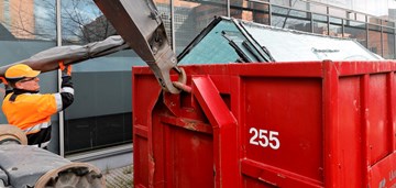 Kierrätettävää lasia merikontissa. Työhenkilö kantaa tavaraa vieressä. Kuvituskuva.