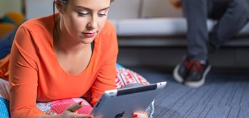 Ihminen makoilee mahallaan lattialla ja katsoo tablettia, kuvituskuva.