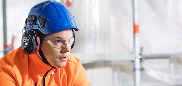 Ihminen työmaakypärä ja suojakuuloimet päällä, kuvituskuva.