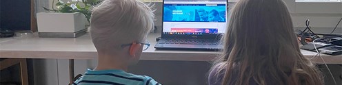Kaksi lasta istuvat tietokoneen näytön edessä pöydän äärellä, kuvituskuva.
